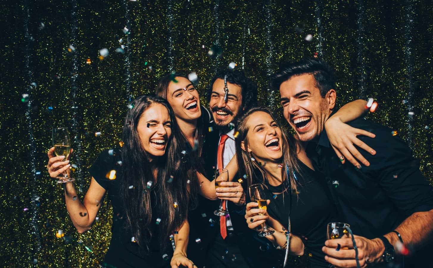 Grupo de amigos brindando con cava en Nochevieja entre confeti dorado