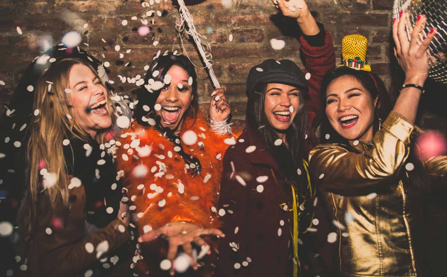 Amigas riendo entre confeti en una fiesta de Nochevieja