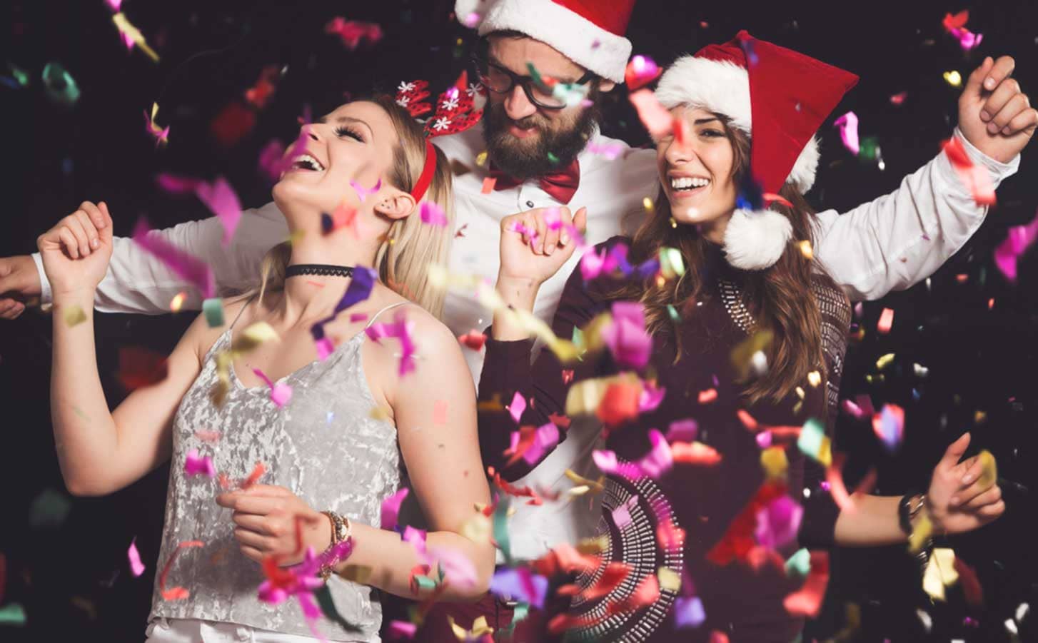 Amigos con gorros navideños celebrando con confeti